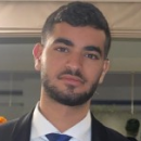 A man with short dark hair and a trimmed beard is wearing a suit and tie, looking at the camera with a neutral expression, ready to attend Cybericon2024.