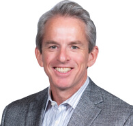 Smiling man with gray hair, wearing a gray blazer over a striped shirt, poses confidently in front of a white background, representing Memcyco at RSA Conference 2025.